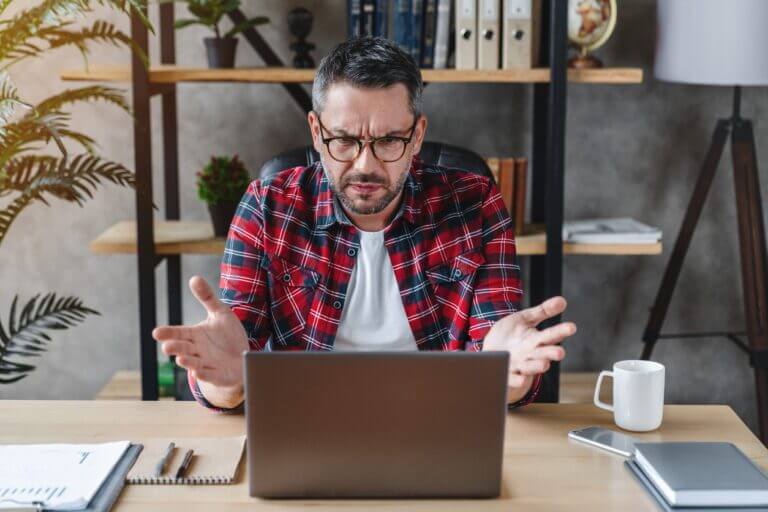 Frustrated man sitting at the desk in home office using computer with low storage space making it slow